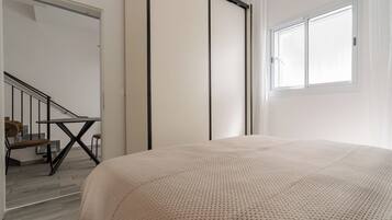 Une chambre à coucher avec un lit, une fenêtre, un escalier et une porte.