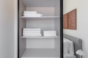 A bathroom with a towel rack holding folded towels, a grey bench, and a wall-mounted lamp.
