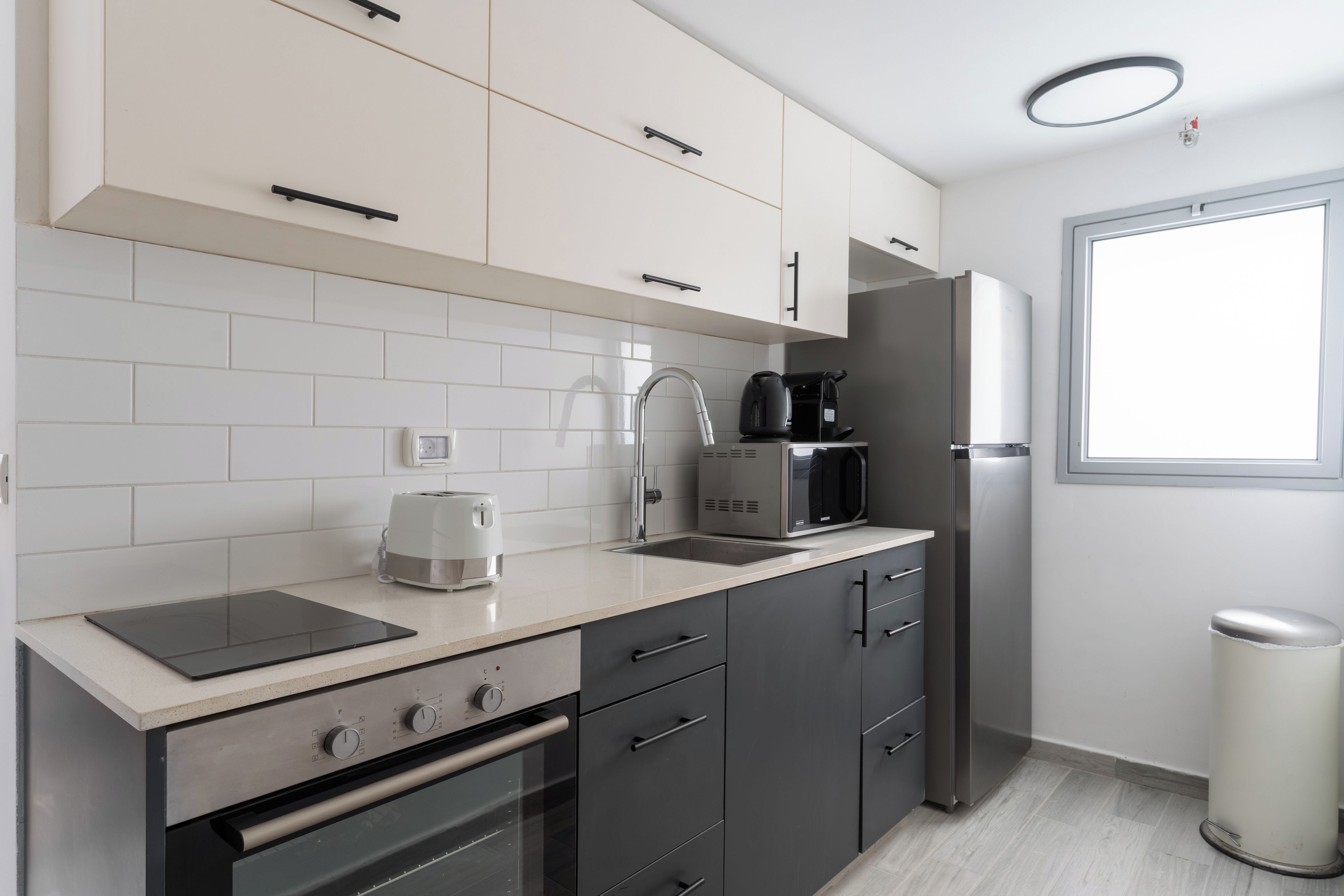 A modern kitchen with white cabinets, a stainless steel refrigerator, a coffee maker, and a toaster.