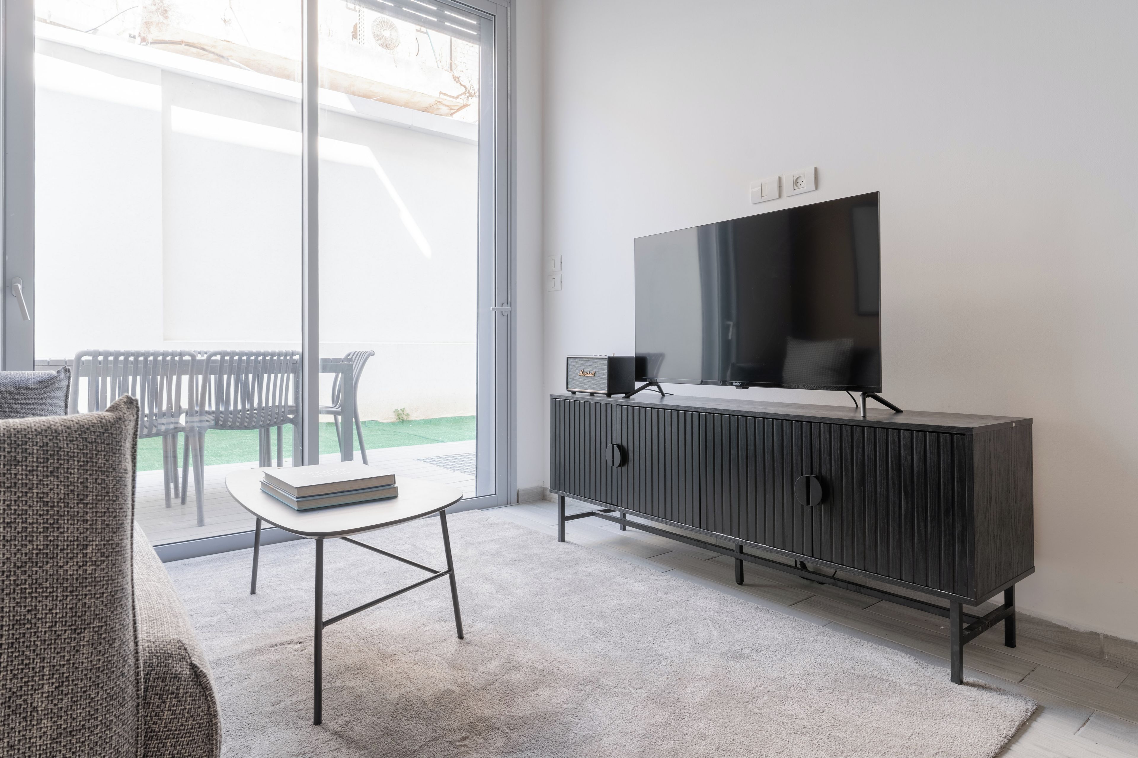 A modern living room with a glass door leading to a balcony, a black entertainment unit, and a white sofa.