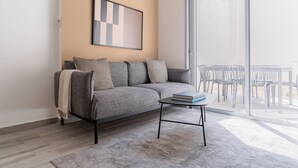 Ein modernes Wohnzimmer mit einem grauen Sofa, gemusterten Kissen, einem kleinen Couchtisch und einem gerahmten abstrakten Kunstwerk an der Wand.