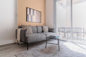 A modern living room with a grey sofa, patterned cushions, a small coffee table, and a framed abstract artwork on the wall. - Blueground Florentine Bright Apartments (Tel Aviv-Yafo)