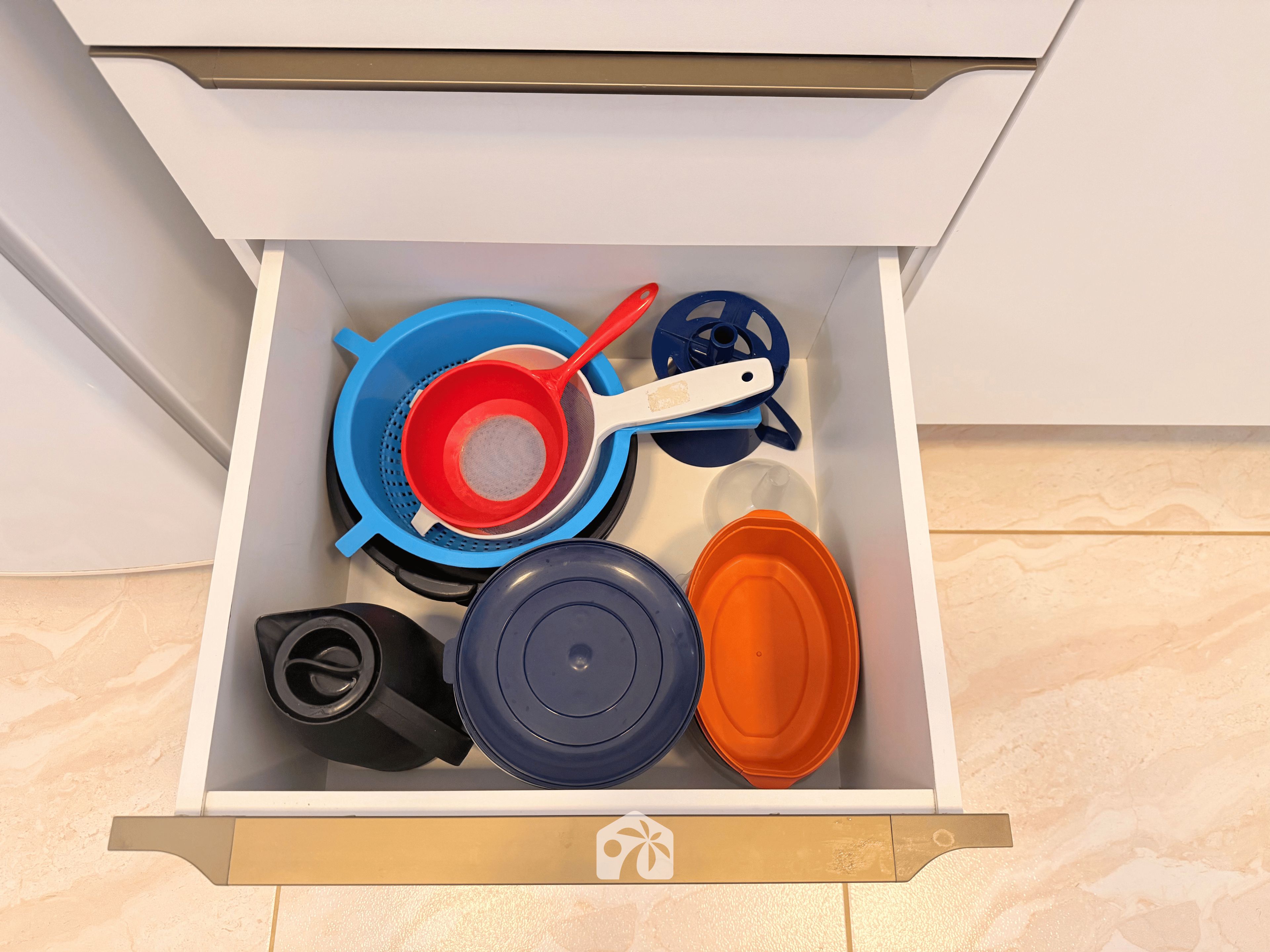 A drawer containing kitchen utensils including a colander, a strainer, and a pot lid.