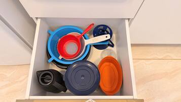 A drawer containing kitchen utensils including a colander, a strainer, and a pot lid.