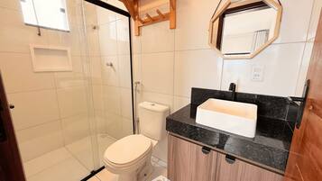 Un baño con ducha, inodoro, lavabo y un estante de madera.