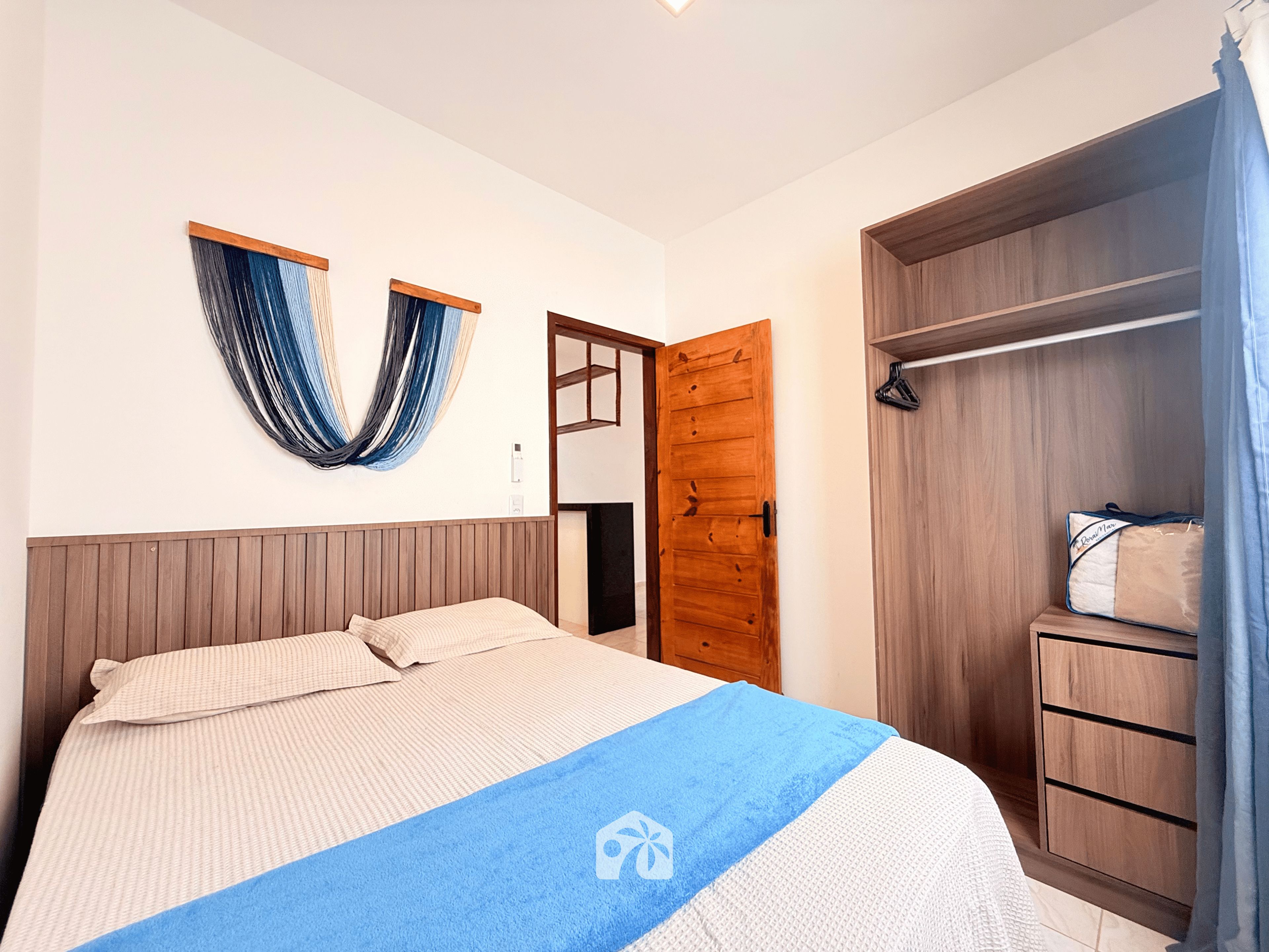 A bedroom with a bed, a wooden wardrobe, a blue towel, and a wall-mounted curtain.