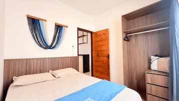 A bedroom with a bed, a wooden wardrobe, a blue towel, and a wall-mounted curtain.