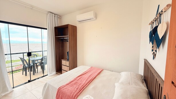 Un dormitorio con cama, armario de madera, balcón con mesa y sillas, y vista al mar.