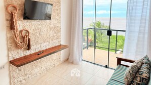Una sala de estar moderna con una pared de piedra, un televisor de pantalla plana, un estante de madera, una guirnalda decorativa de cuentas y un balcón con vistas al mar.