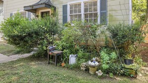 Un giardino residenziale con diverse piante, un tavolino e una casetta decorativa per uccelli.