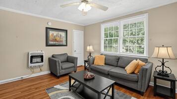 A living room with a gray sofa, a coffee table, a fireplace, a ceiling fan, and a window with blinds.