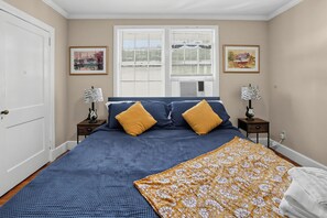 A bedroom with a bed, two nightstands, a window with blinds, and two wall-mounted lamps.