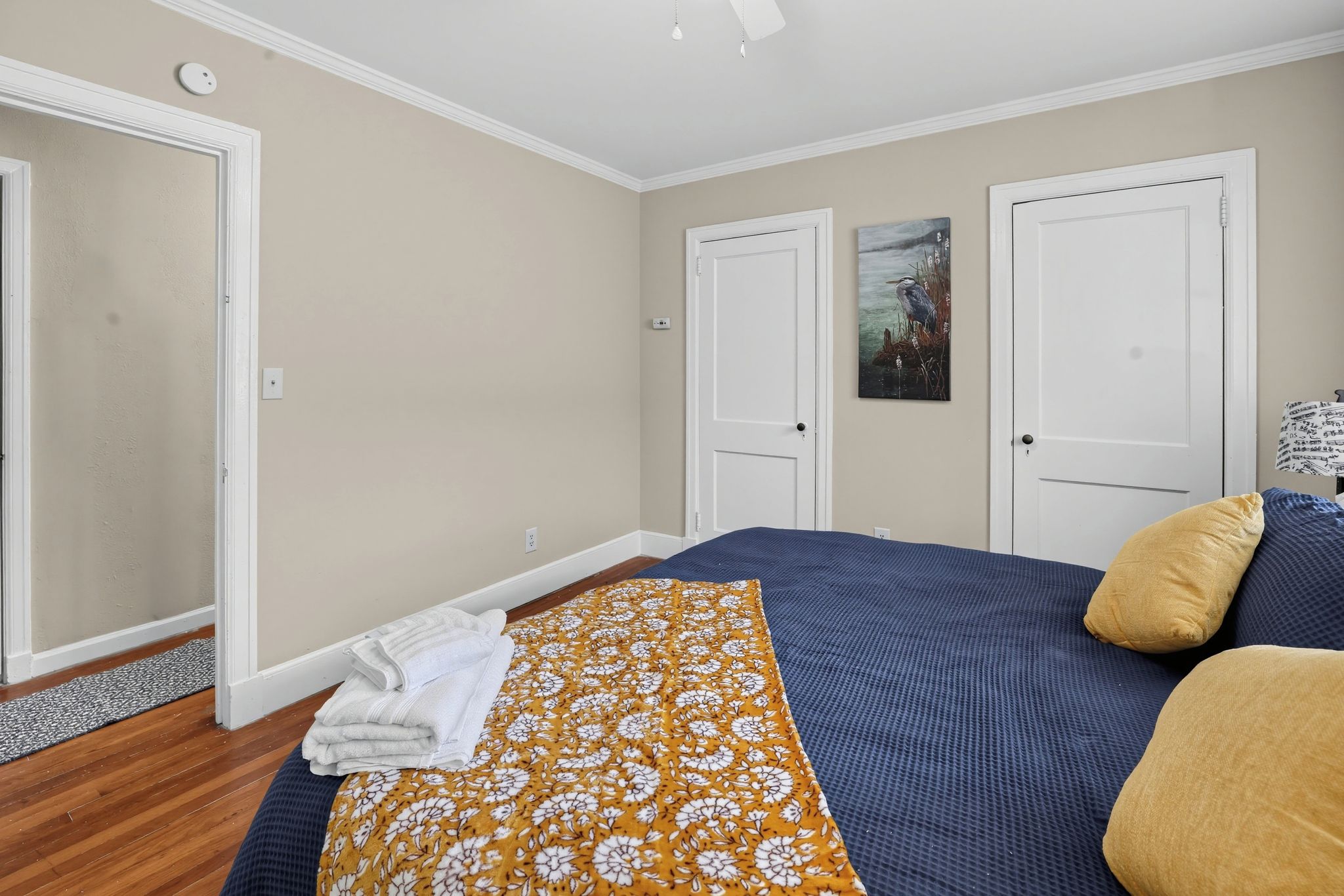 Un dormitorio con cama, puerta, un cuadro colgado en la pared y una lámpara de noche.