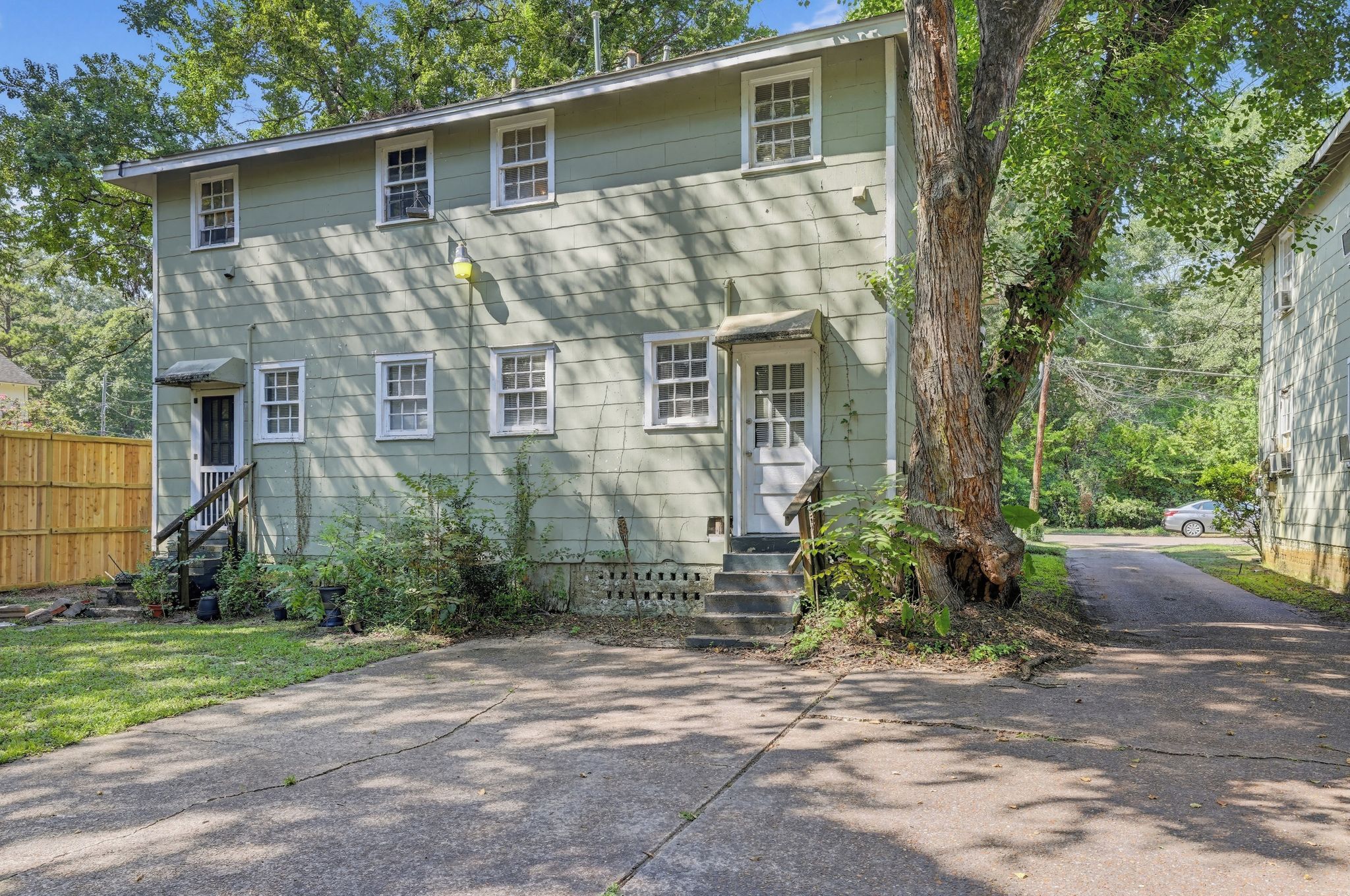 A two-story house with a front porch, a wooden fence, and a tree in the yard.