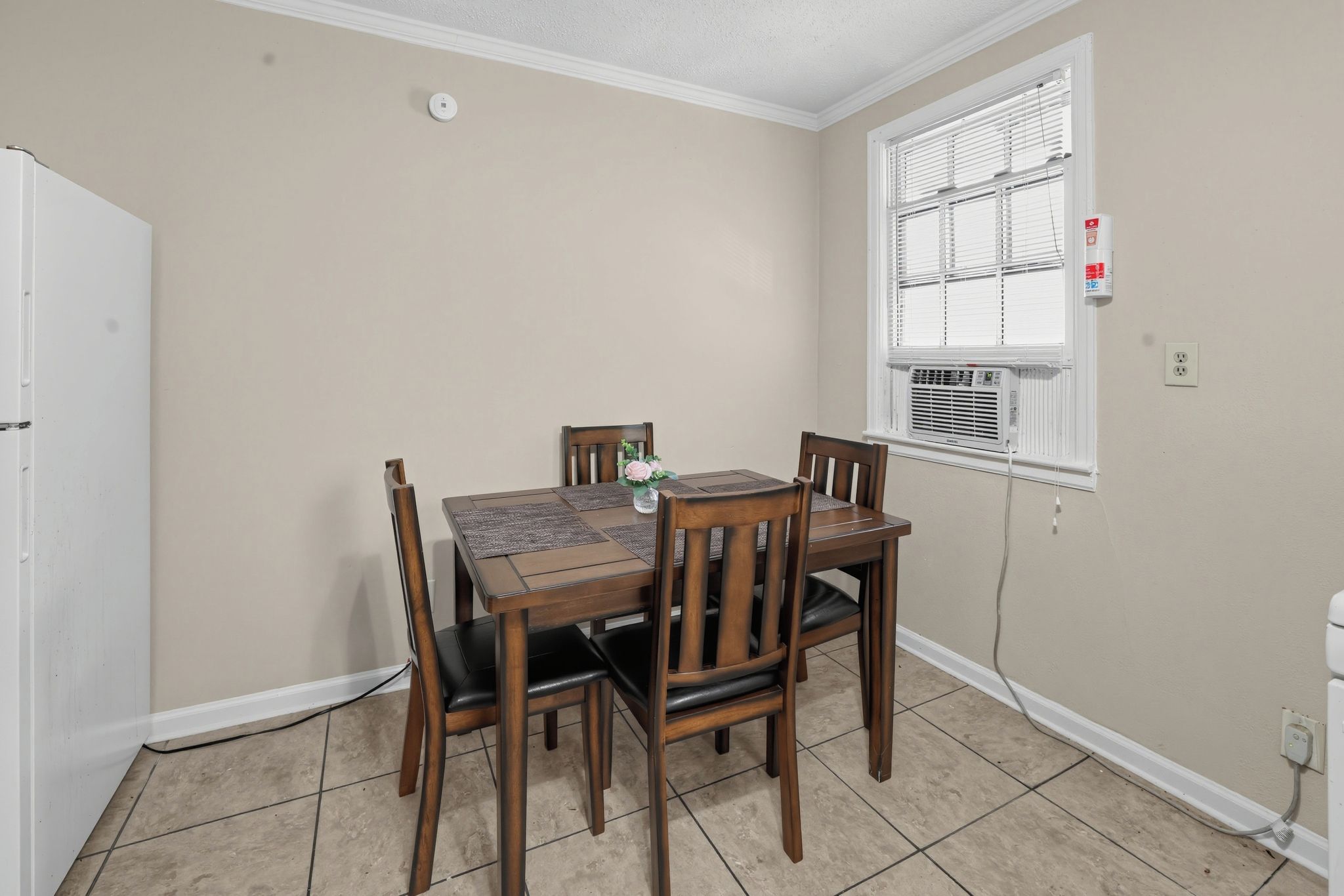 A dining area with a table and chairs, a window with blinds, and a wall-mounted air conditioner.