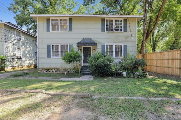 A two-story house with a front door, two windows on each floor, a small porch, and a wooden fence.