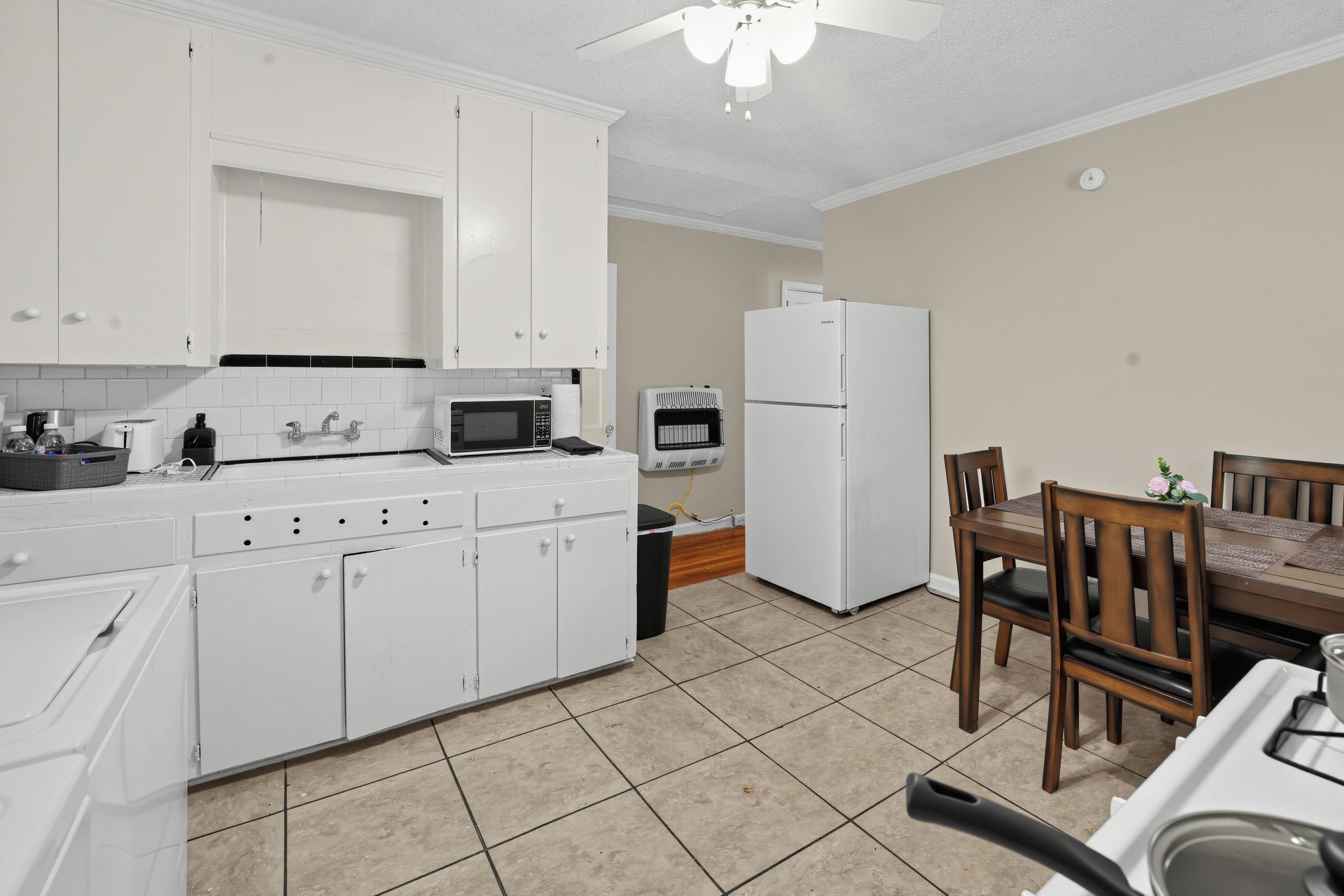 A compact kitchen with white cabinets, a microwave, a refrigerator, and a dining area with a table and chairs.