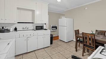 A compact kitchen with white cabinets, a microwave, a refrigerator, and a dining area with a table and chairs.
