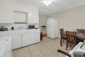 A compact kitchen with white cabinets, a microwave, a refrigerator, and a dining area with a table and chairs. - Old Cloverdale Cozy Nest (Montgomery)