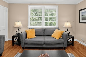 A living room with a grey sofa, two lamps, a window with blinds, and a framed picture on the wall. - Old Cloverdale Cozy Nest (Montgomery)