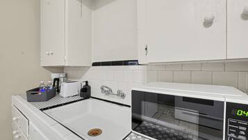 A kitchen with white cabinets, a microwave, a sink, and a small countertop with a kettle and a basket.