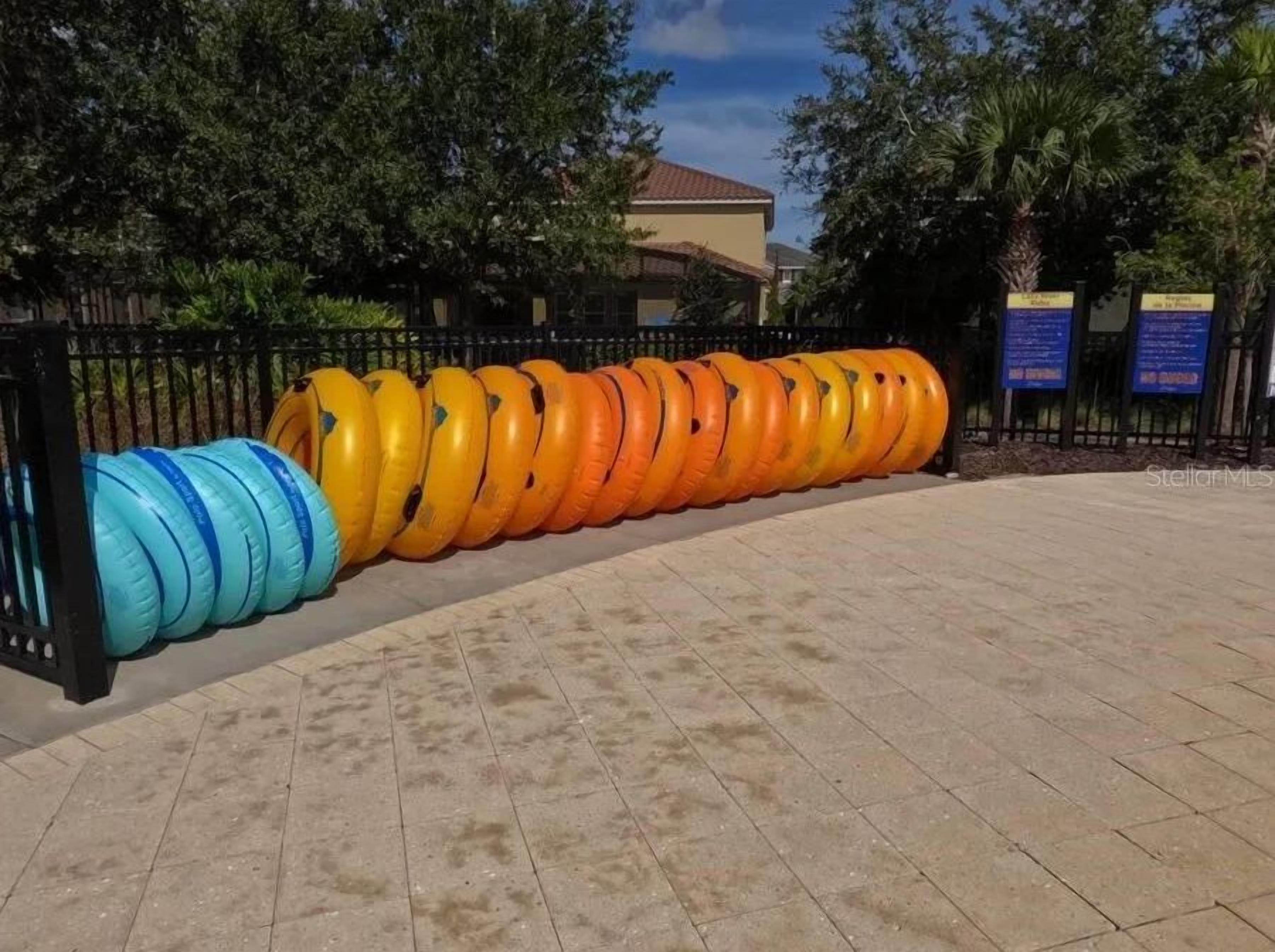 A row of colorful inflatable rings arranged in a line on a paved area, with a fence and trees in the background.