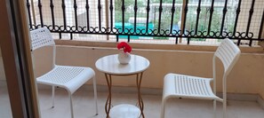 Un balcó amb dues cadires de plàstic blanc i una taula rodona petita, un vas de ceràmica blanc amb una flor vermella, i una tanca metàl·lica.
