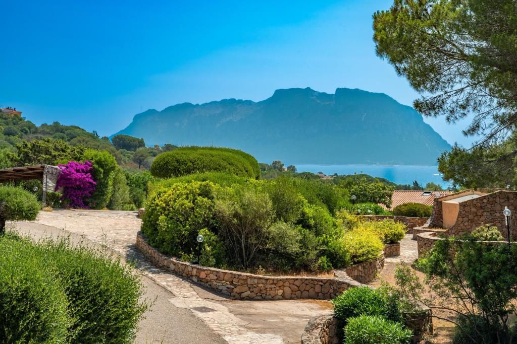 Un sentier de pierre mène à un jardin luxuriant, d’où l’on peut admirer une vue sur la montagne et la mer.