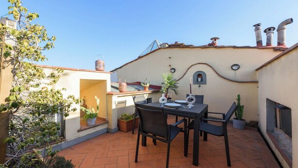 Eine Terrasse im Freien mit einem Tisch für zwei Personen, umgeben von Topfpflanzen und blauem Himmel.