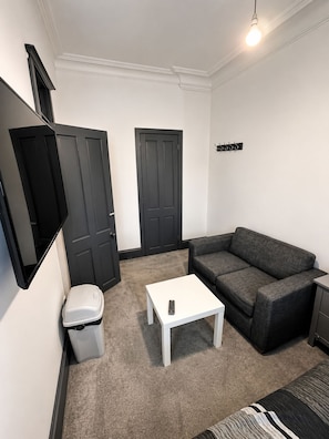 A room with a white sofa, a white coffee table, a black trash bin, and a black door. - Brilliant 2-bedroom apartment in Glasgow perfect for your stay (Glasgow)