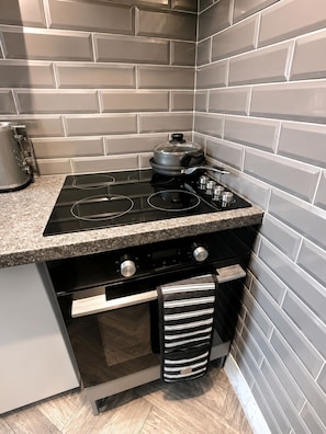 A kitchen with a black stovetop, a pot on the burner, a kettle, and a striped towel hanging from the oven handle. - Brilliant 2-bedroom apartment in Glasgow perfect for your stay (Glasgow)