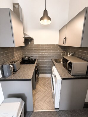 A compact kitchen with grey cabinets, a microwave, a washing machine, and a kettle. - Brilliant 2-bedroom apartment in Glasgow perfect for your stay (Glasgow)