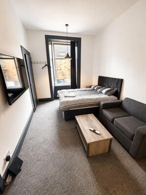 A modern bedroom with a bed, a sofa, a wooden coffee table, and a TV on the wall. - Brilliant 2-bedroom apartment in Glasgow perfect for your stay (Glasgow)