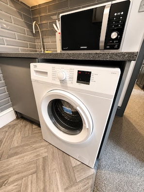 A front-loading washing machine with a digital display, a microwave above it, and a tiled backsplash. - Brilliant 2-bedroom apartment in Glasgow perfect for your stay (Glasgow)