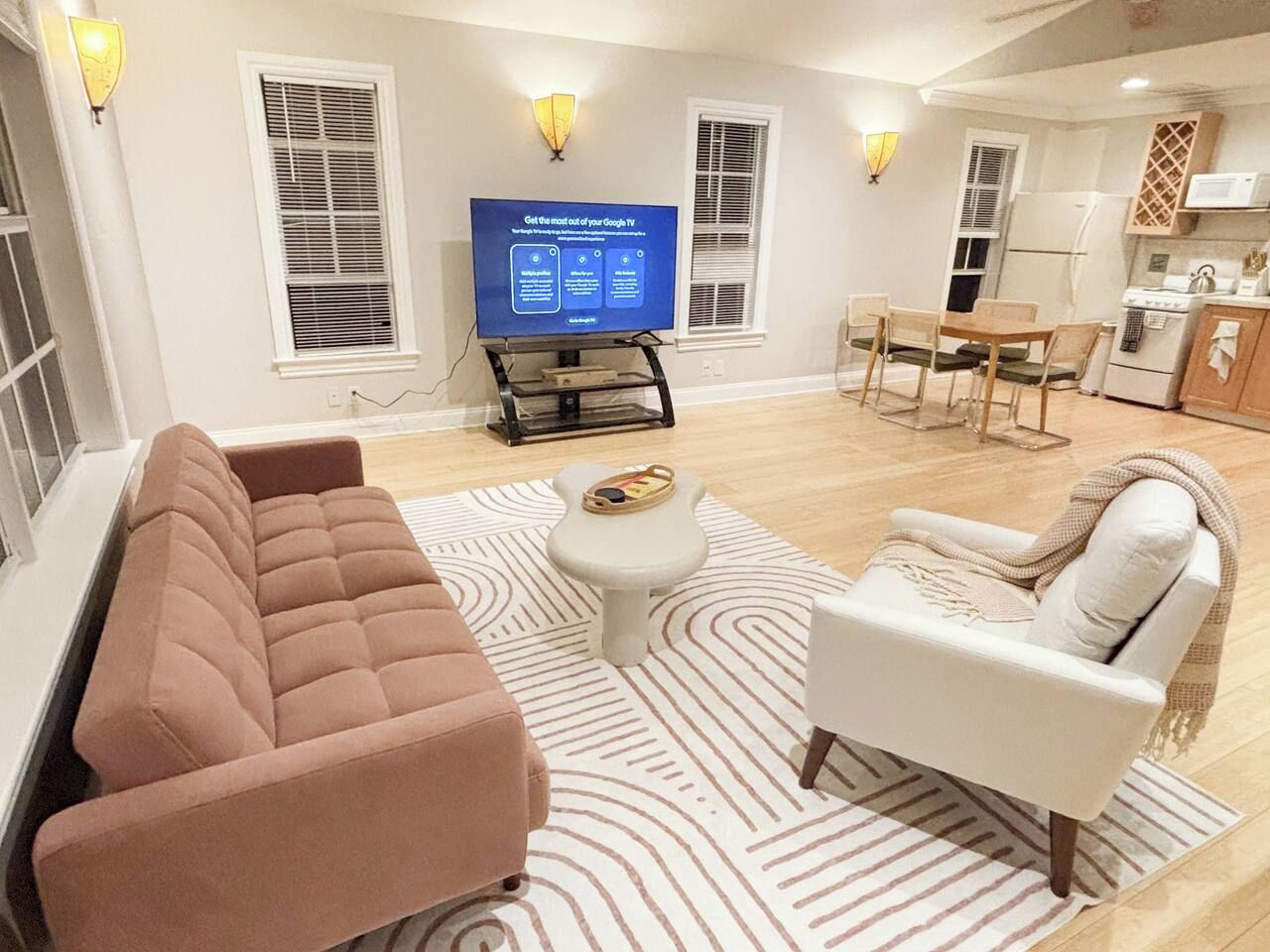 A living room with a sofa, armchair, coffee table, and a flat-screen TV on a stand.