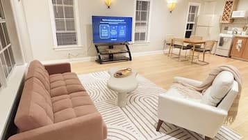 A living room with a sofa, armchair, coffee table, and a flat-screen TV on a stand.