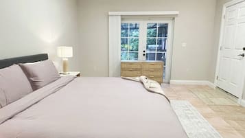 Quarto com cama, mesa de cabeceira, abajur, cômoda e porta que dá para uma varanda.