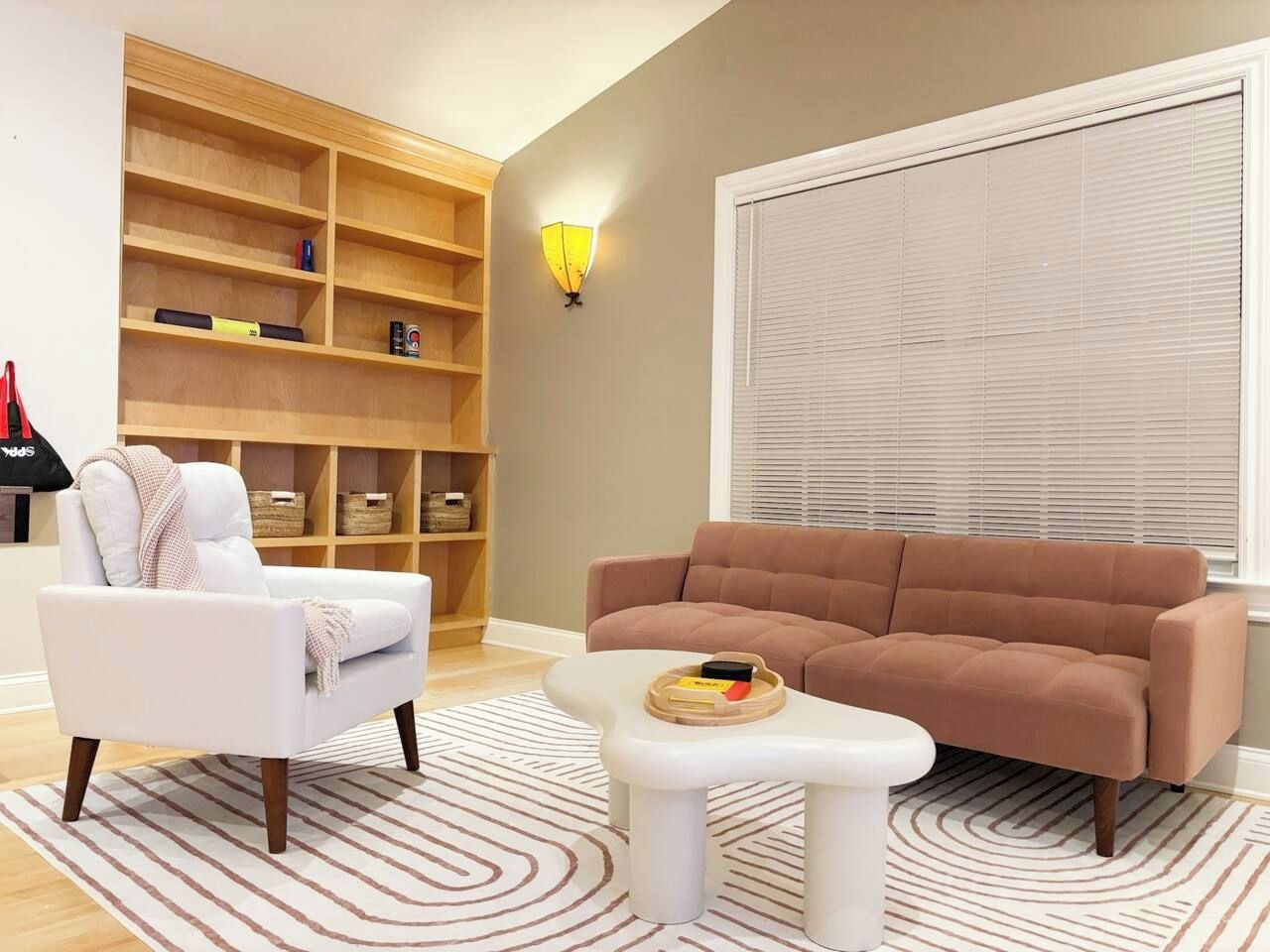 Un salon avec un fauteuil blanc, un canapé marron, une table basse blanche et une étagère en bois avec des paniers.