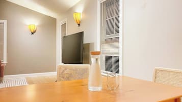 Uma área de refeições com uma mesa de madeira, duas cadeiras de vime, uma garrafa de água e duas luminárias fixadas na parede.