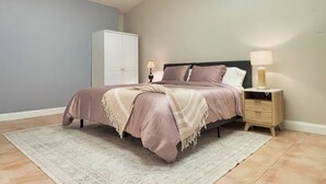 Een slaapkamer met een bed, nachtkastje, lamp en een kledingkast.
