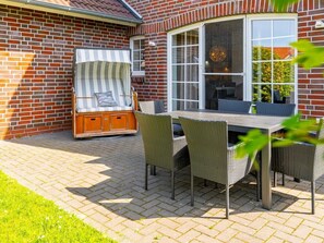 A patio with a table and chairs, a cushioned bench, and a brick wall. - Holiday Home in Greetsiel With Terrace (Krummhoern)