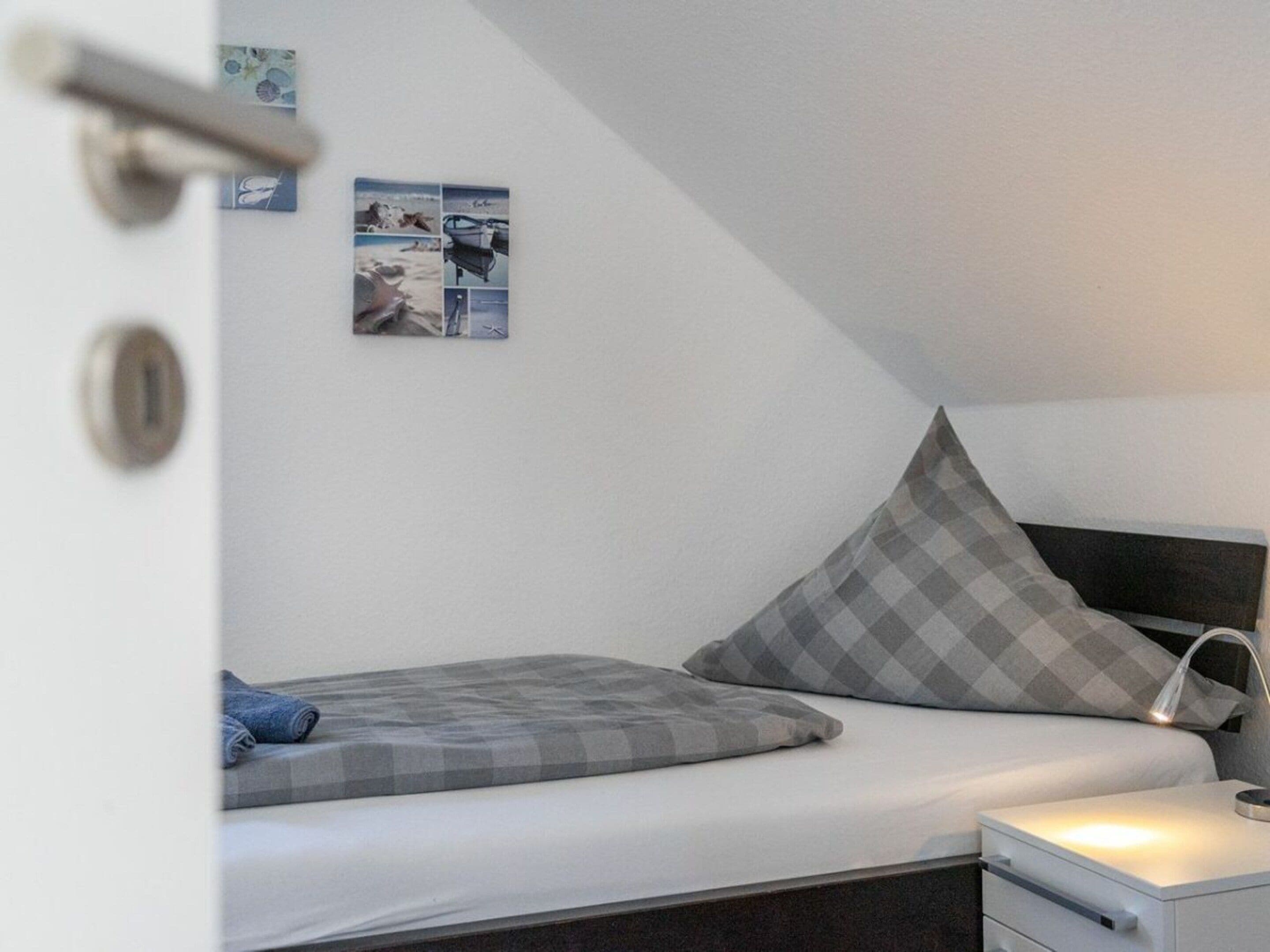 A bedroom with a bed, a nightstand, a lamp, and a wall with pictures.