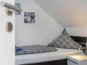 A bedroom with a bed, a nightstand, a lamp, and a wall with pictures. - Holiday Home in Greetsiel With Terrace (Krummhoern)
