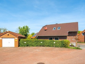 A residential building with a brick facade, a garage, and a well-maintained hedge. - Holiday Home in Greetsiel With Terrace (Krummhoern)