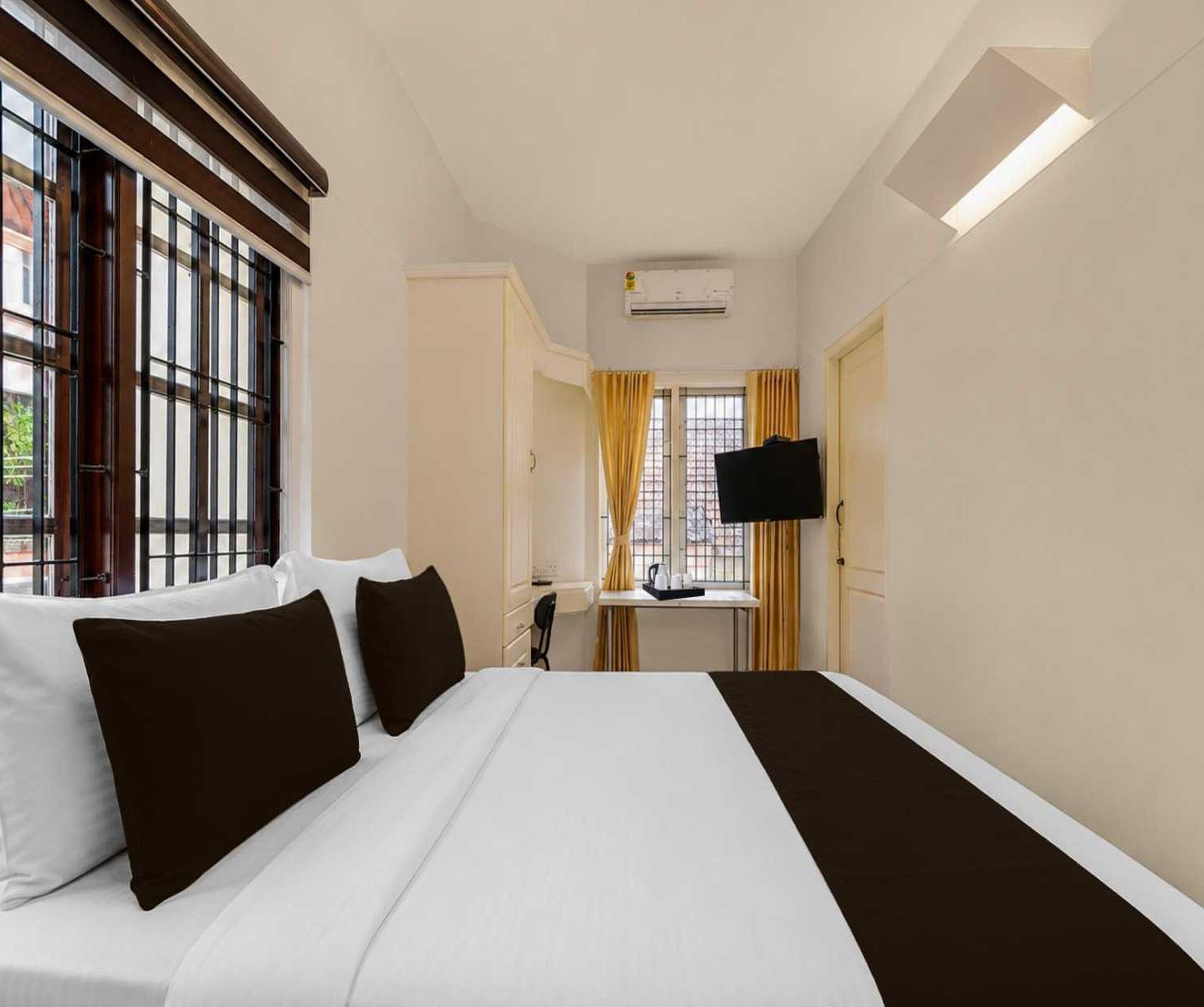 Una camera d'albergo con un letto, una scrivania, una televisione e una finestra con persiane.