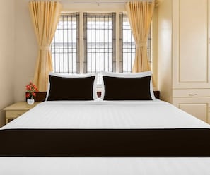 Una camera d'albergo con un letto grande, due cuscini neri, una coperta bianca e tende beige.