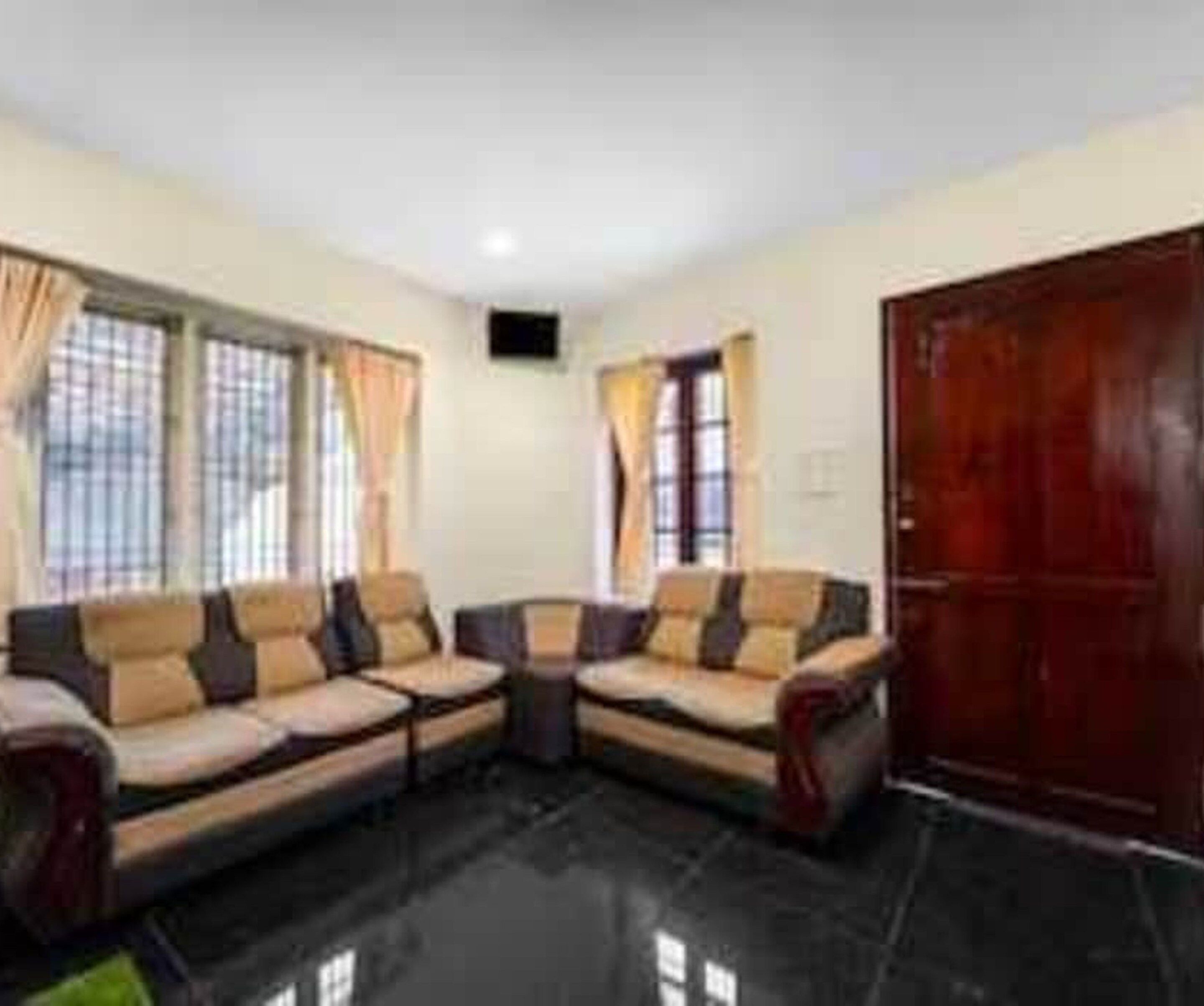 A living room with a sectional sofa, a wooden door, and large windows with curtains.