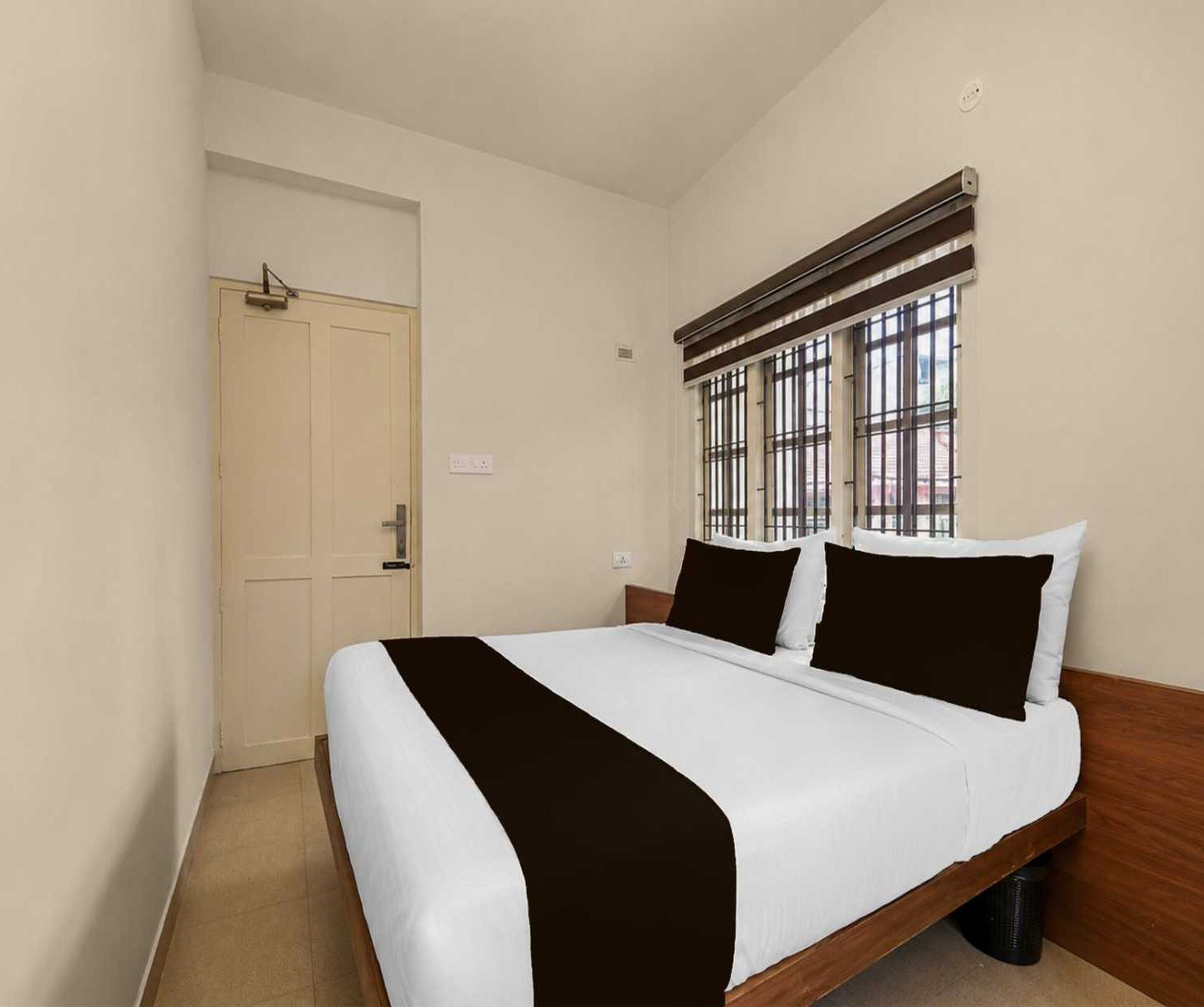 Une chambre d’hôtel avec un lit simple, une porte et une fenêtre avec des barreaux.