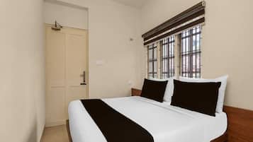 Une chambre d’hôtel avec un lit simple, une porte et une fenêtre avec des barreaux.