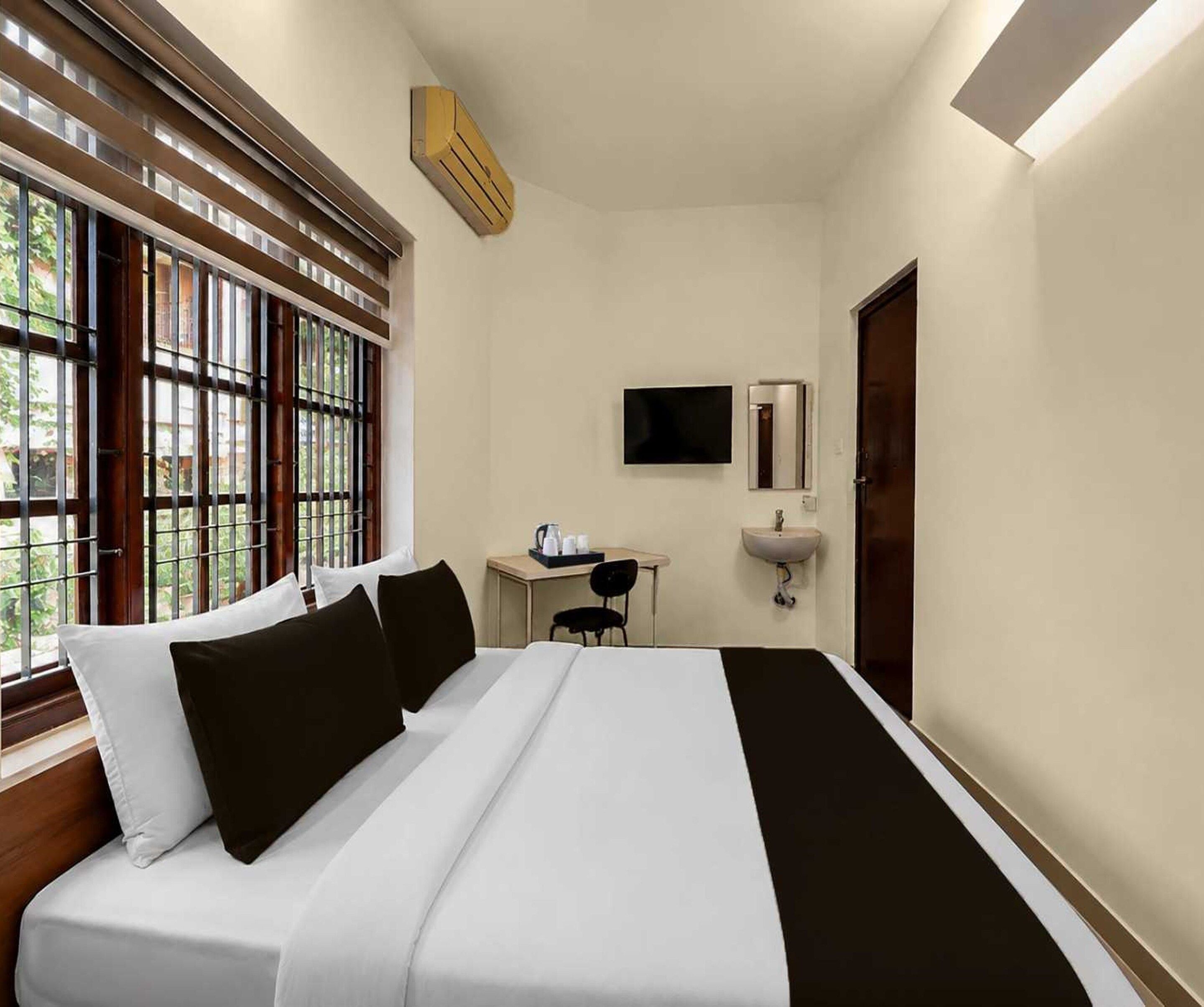 Una camera d'albergo con un letto, una scrivania con una sedia, una televisione, un lavandino e una finestra con persiane.